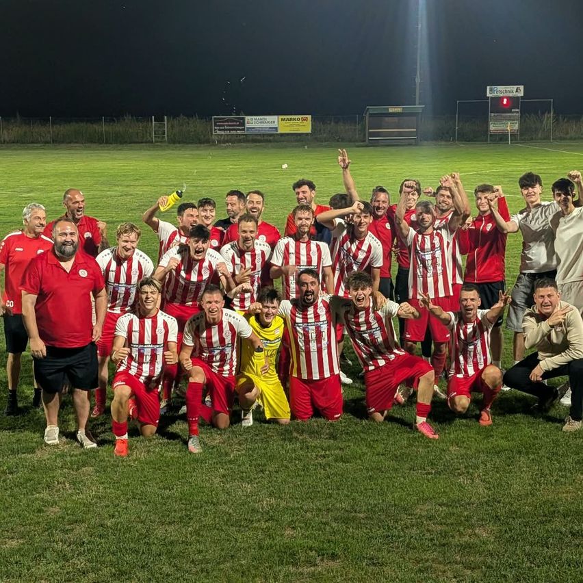 A soccer team celebrates on a field at night, with players in red and white striped jerseys, one holding a bottle.