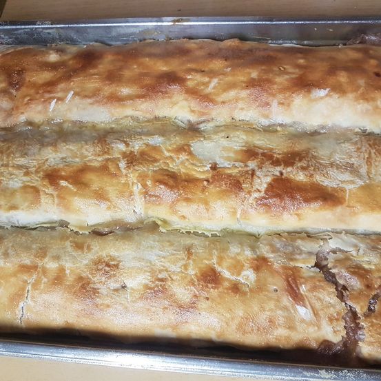 Drei goldbraune Gebäckstücke sind in einem Backblech angeordnet, mit sichtbaren Falten und einem leicht angebrannten Rand. Sie sehen frisch gebacken aus und sind bereit zum Servieren.