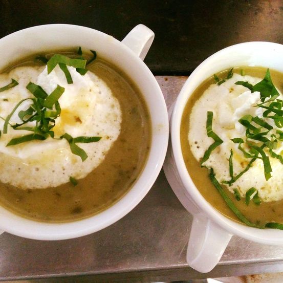 Zwei weiße Suppenschüsseln mit cremigen Toppings, garniert mit grünen Kräutern. Die Suppe hat eine helle, grüne Farbe.