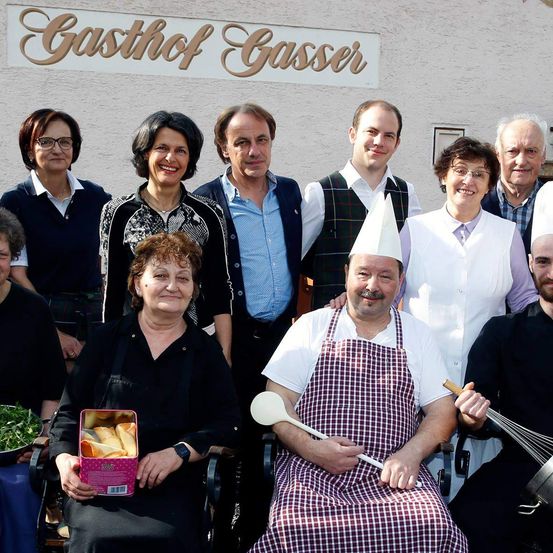 Eine Gruppe von Menschen posiert für ein Foto vor einem Gebäude namens Gasthof Gasser. Sie alle lächeln.