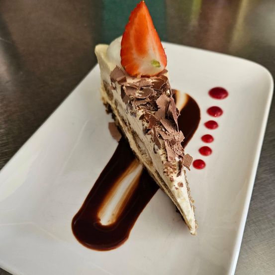 Ein Stück Kuchen mit Schokolade und Erdbeere auf einem weißen Teller. Schokoladensauce und rote Punkte sind auf dem Teller.