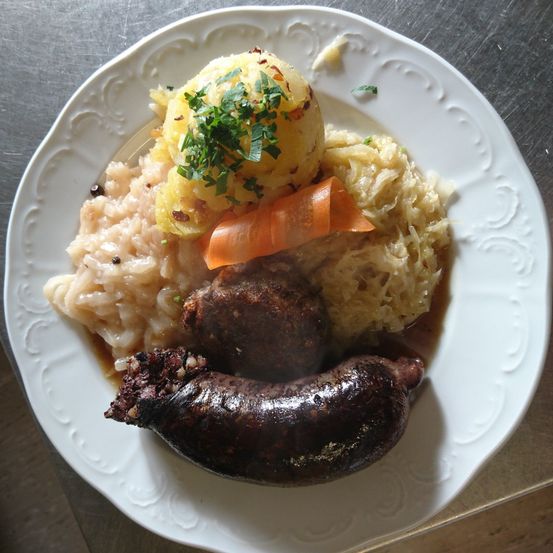 Ein weißer Teller mit einem Gericht aus Würsten, Reis, Sauerkraut und Karotten mit Petersilie obenauf.