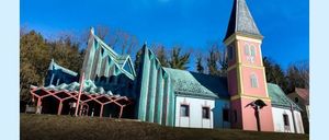 Eine Kirche mit einem Kirchturm und einem grünen Dach wird mit dem Text 'Dem Himmel nah!' auf einem blauen Hintergrund gezeigt.