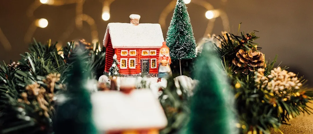 Ein festliches Miniatur-Rothaus mit Schnee auf dem Dach steht in einer Weihnachtsszene, umgeben von grünen Bäumen und kleinen dekorativen Lichtern.