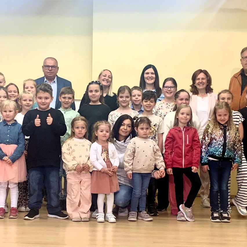 Eine Gruppe von Kindern und Erwachsenen posiert für ein Foto in einem Raum. Sie stehen lächelnd in einer Reihe. Ein Kind gibt einen Daumen hoch.