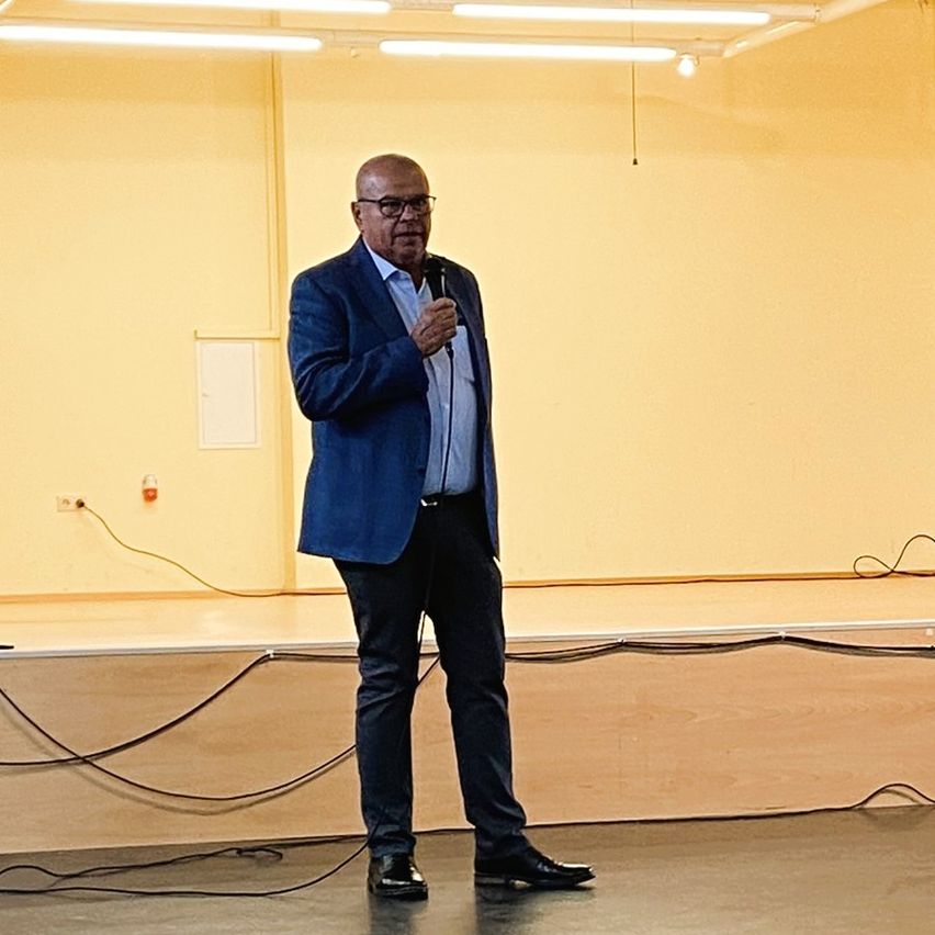 Ein Mann in einem blauen Anzug steht mit einem Mikrofon auf der Bühne und hält möglicherweise eine Rede in einem Konferenzraum.