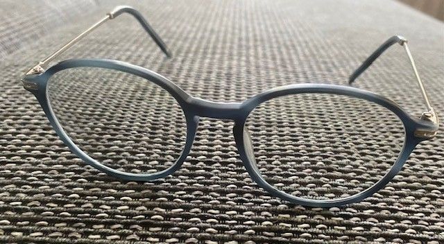 Ein Paar runde Brille mit silberfarbenen Metallbügeln und klaren Gläsern, die auf einer strukturierten Oberfläche liegt.