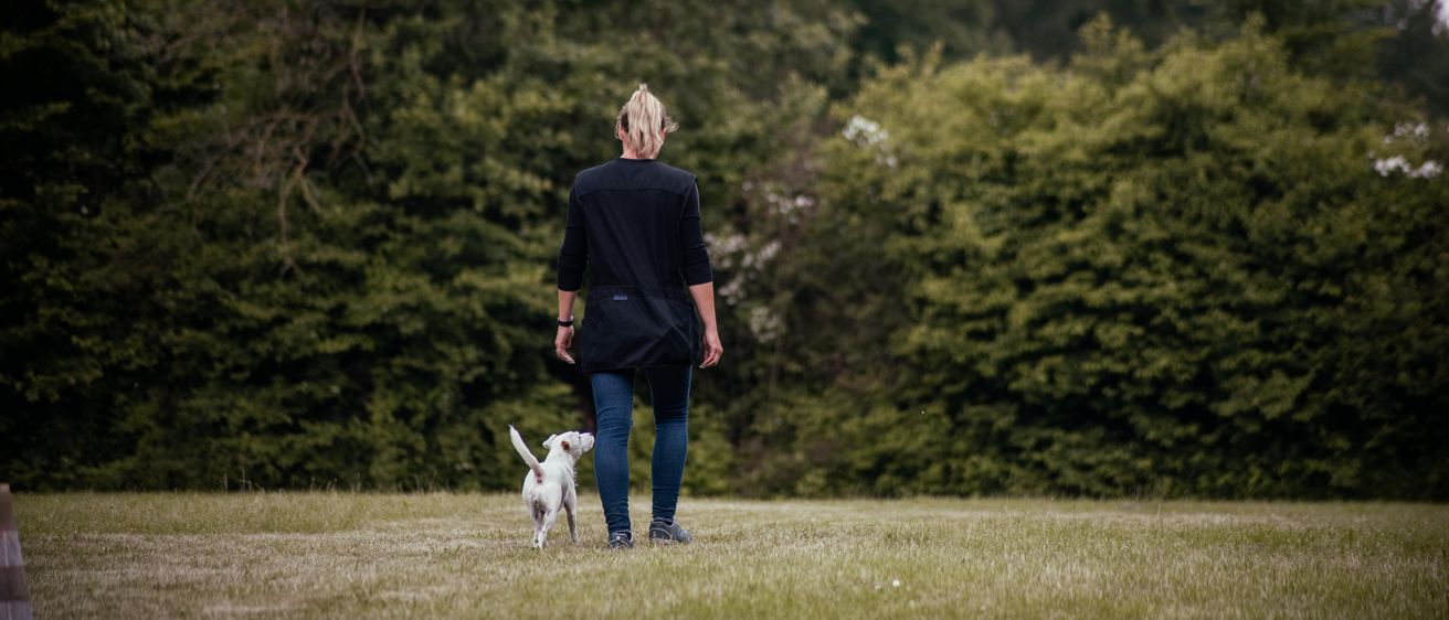 Bild enthält, Person, Walking, Grass, Pants, Coat, Canine, Dog, Pet, Jeans, Tree