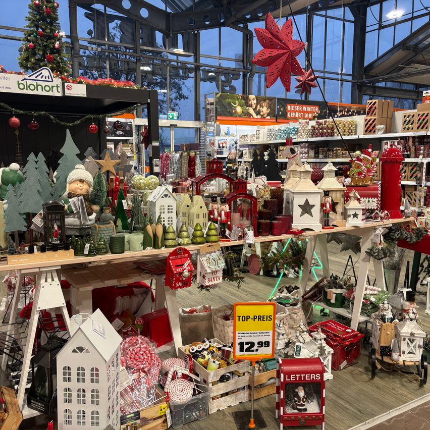 A shop interior with Christmas decorations on display. Various items like Christmas trees, houses, candles, and more are arranged on a table. A sign with the text 'Top-Preis' and the price '12.99' is visible.