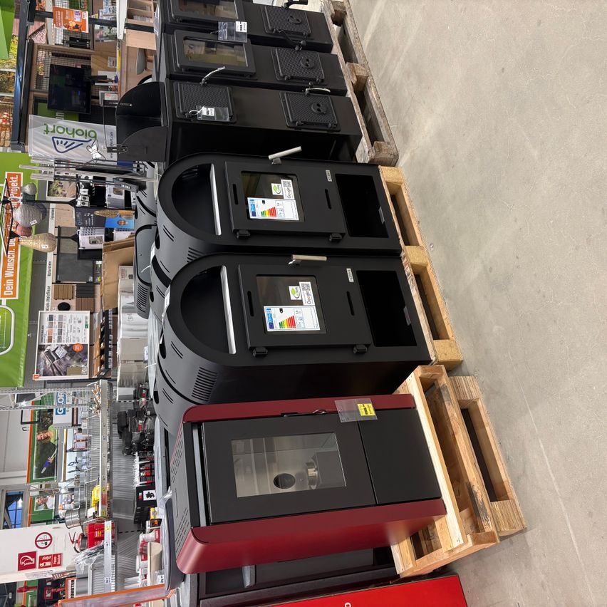 An overhead view of a warehouse with several black and red fireplaces stacked on wooden pallets. The pallets are arranged in a row.