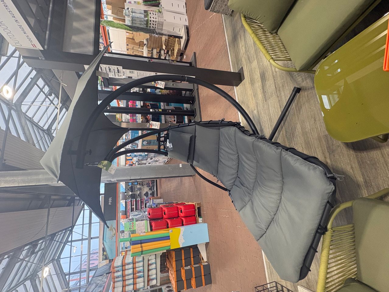 An overhead view of a hanging chair with a black frame and gray cushions in a store. Behind it are various items and products on shelves.
