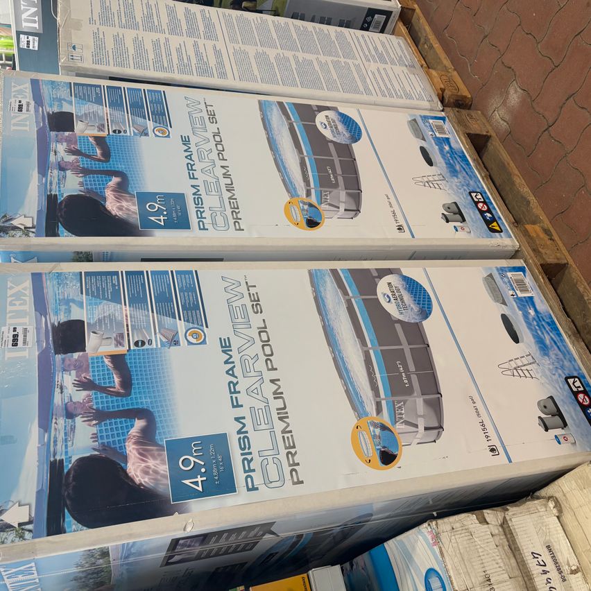 Stacked boxes of Intex Prism Frame Premium Pool Set are on display. Each box features a blue and white design with the product name and specifications.