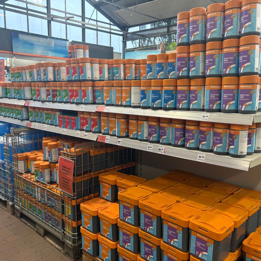 A store with multiple shelves displaying various packs of Quattro Tabs, a cleaning product, with orange lids and different colors, in front of a glass wall.