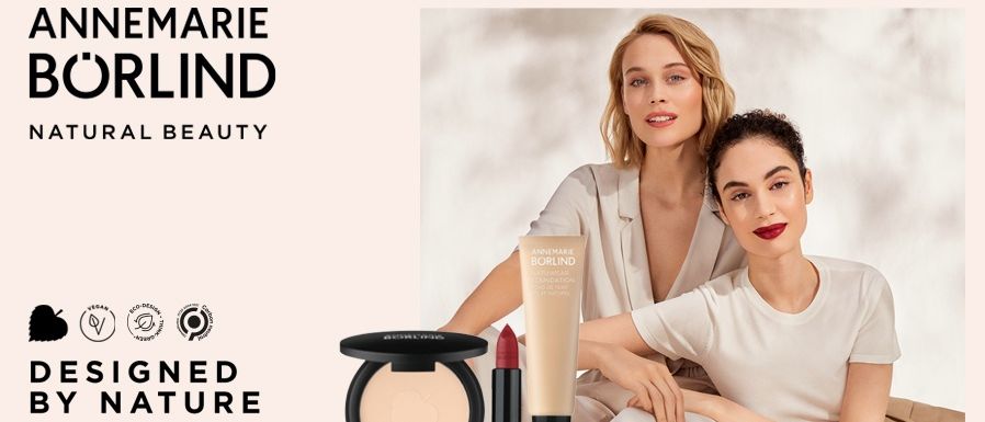 Annmarie Borlind stellt eine Kollektion natürlicher Schönheitsprodukte vor, einschließlich Foundation, Lippenstift und Puderkompakt. Zwei Frauen sind in der Werbung zu sehen, eine mit rotem Lippenstift.