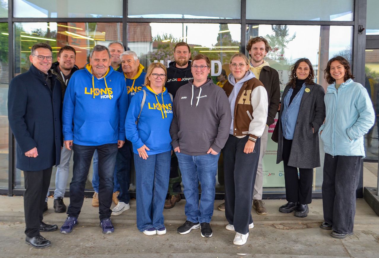 Eine Gruppe von Personen, alle in blauen Hoodies, versammelt sich für ein Foto vor einem Gebäude. Sie scheinen zu lächeln und posieren für die Kamera.