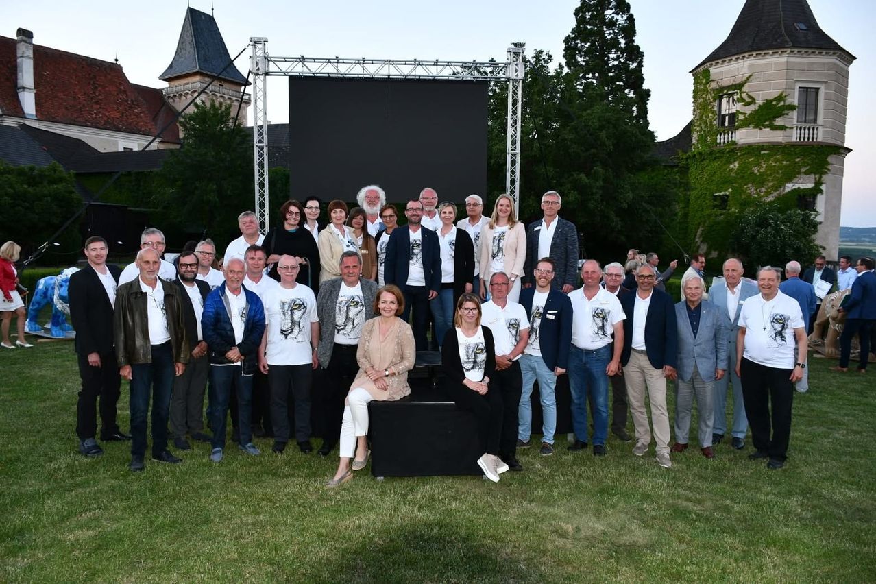 Eine Gruppe von Menschen, die weiße T-Shirts mit Tigeraufdruck tragen, steht vor einer großen Leinwand auf einem Rasen.
