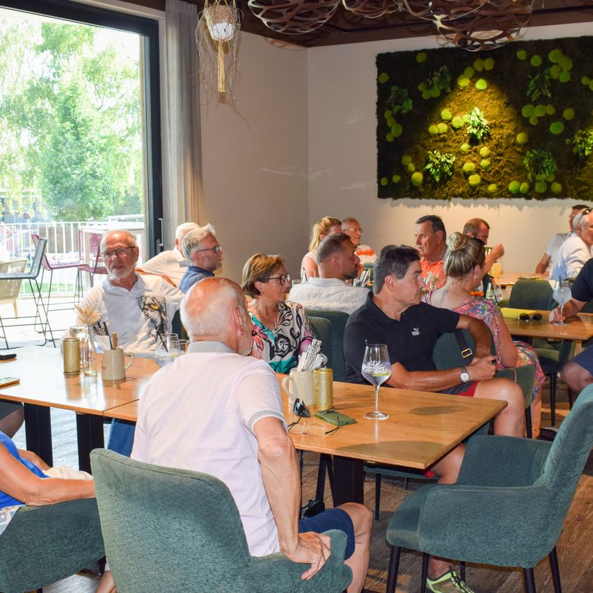 Eine Gruppe von Menschen sitzt an Tischen in einem Restaurant mit einer grünen Wand im Hintergrund.