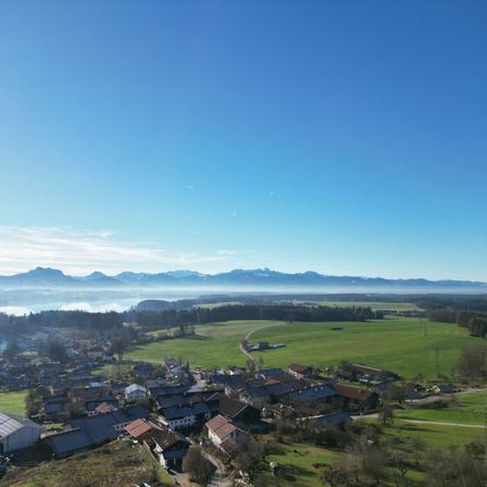 Luftaufnahme eines kleinen Dorfes mit grünen Feldern und Bergen in der Ferne.