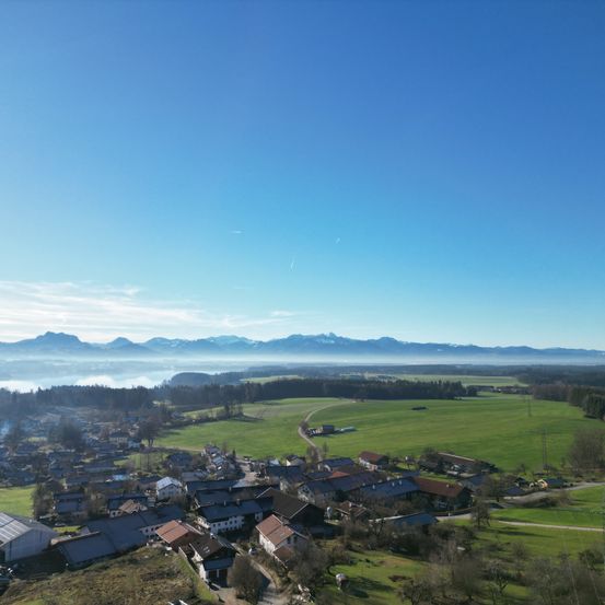 Luftaufnahme eines kleinen Dorfes mit grünen Feldern und Bergen in der Ferne.