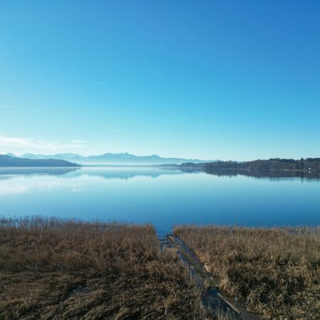 Ein ruhiger See mit ruhigen Wassern, die den blauen Himmel und die entfernten Berge unter einem klaren Himmel widerspiegeln.