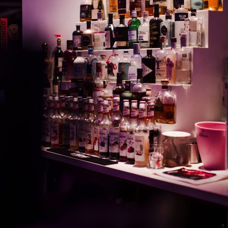 Eine Bartheke mit vielen Flaschen von Likör, Spirituosen und Sirupen auf mehreren Regalen und einer Arbeitsplatte.