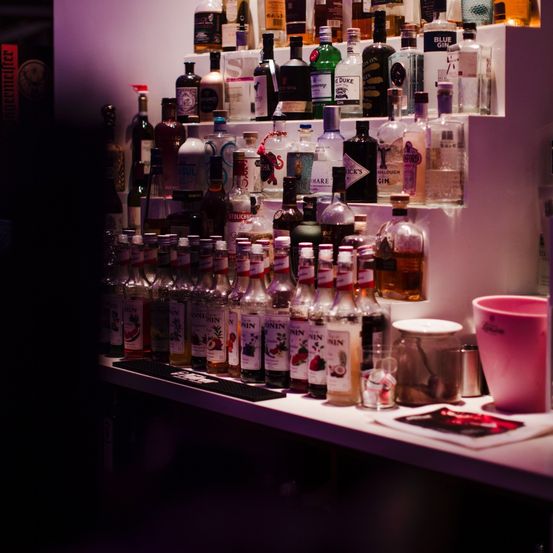 Eine Bartheke mit vielen Flaschen von Likör, Spirituosen und Sirupen auf mehreren Regalen und einer Arbeitsplatte.