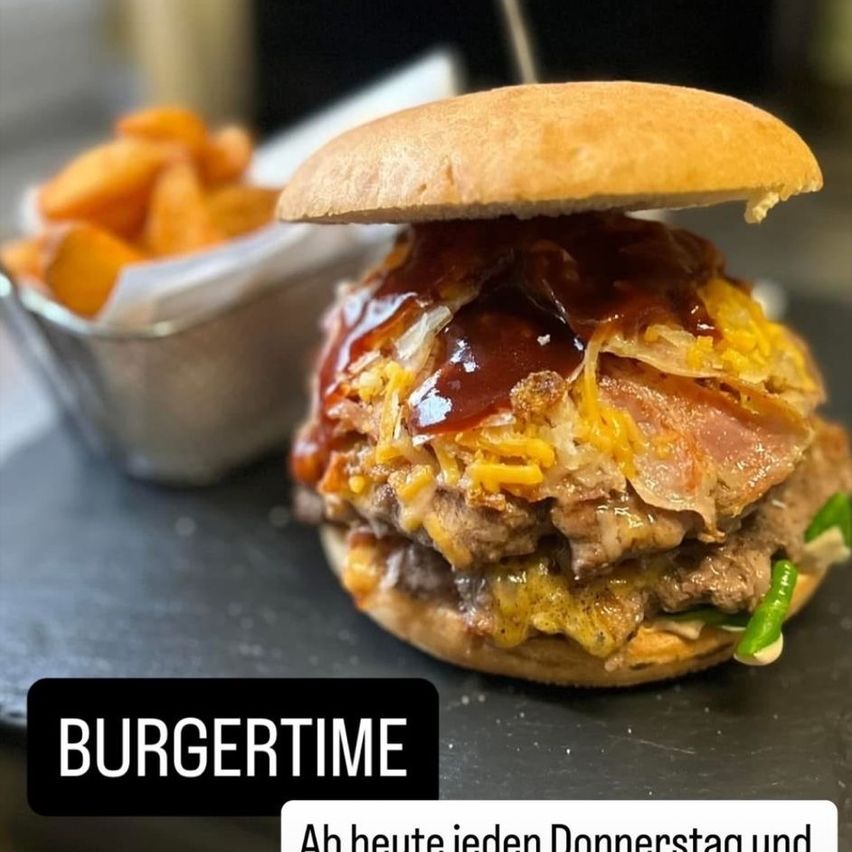 A burger with a variety of toppings, including cheese, bacon, and a green pepper, placed on a table with a bowl of fries. The words Burgertime are displayed below.