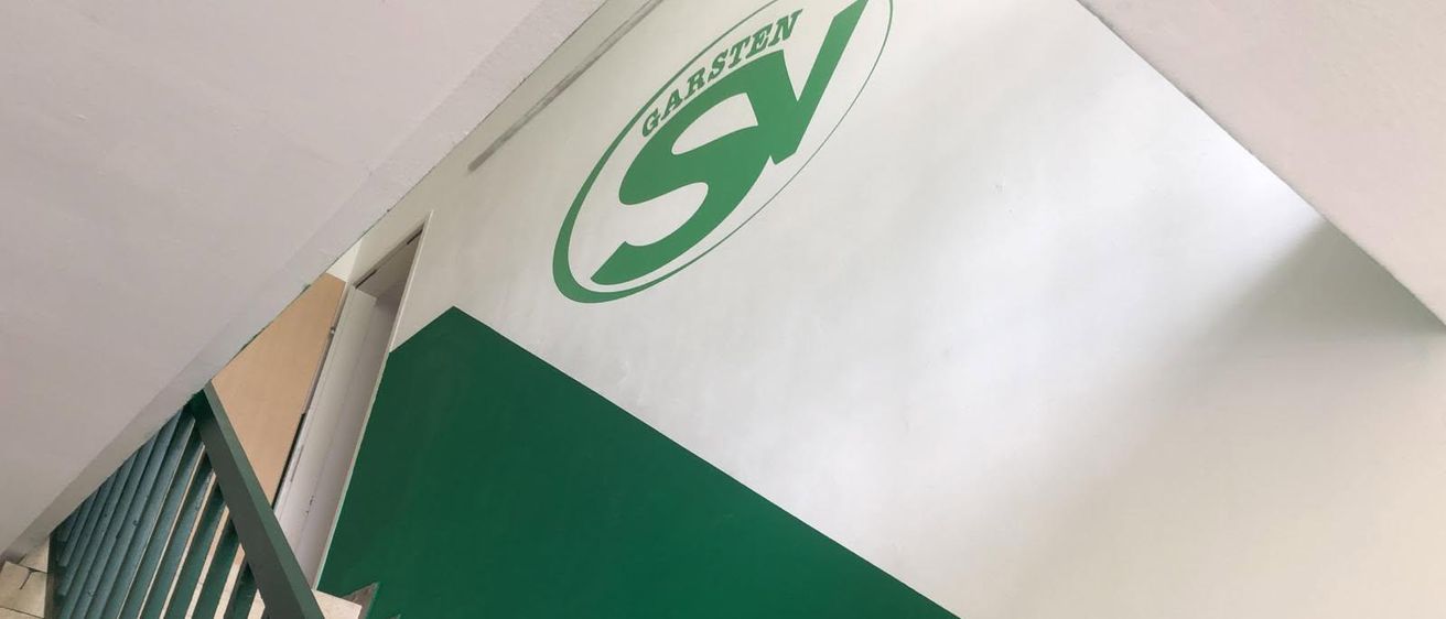 Eine weiße und grüne Wandecke zeigt das Logo von 'SV Garsten'. Das Logo ist kreisförmig und zeigt die Buchstaben 'SV' in Grün mit einem weißen Umriss.