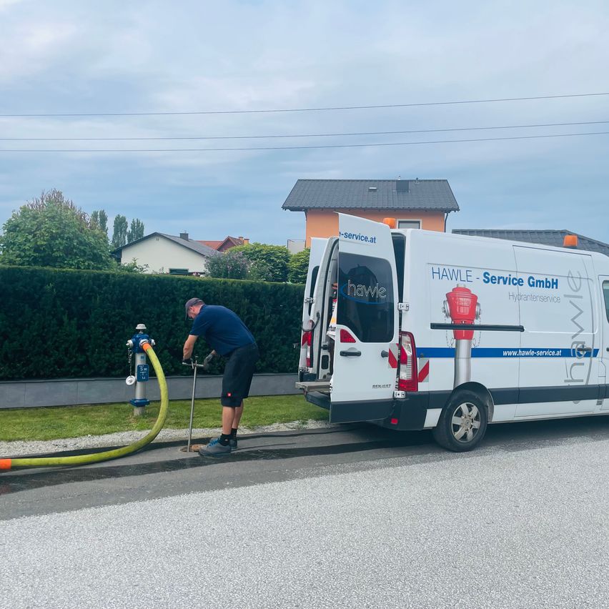 Ein Mann benutzt ein Werkzeug, um an einem Feuerhydranten zu arbeiten, während ein weißer Van mit dem Wort Hawle geparkt ist.
