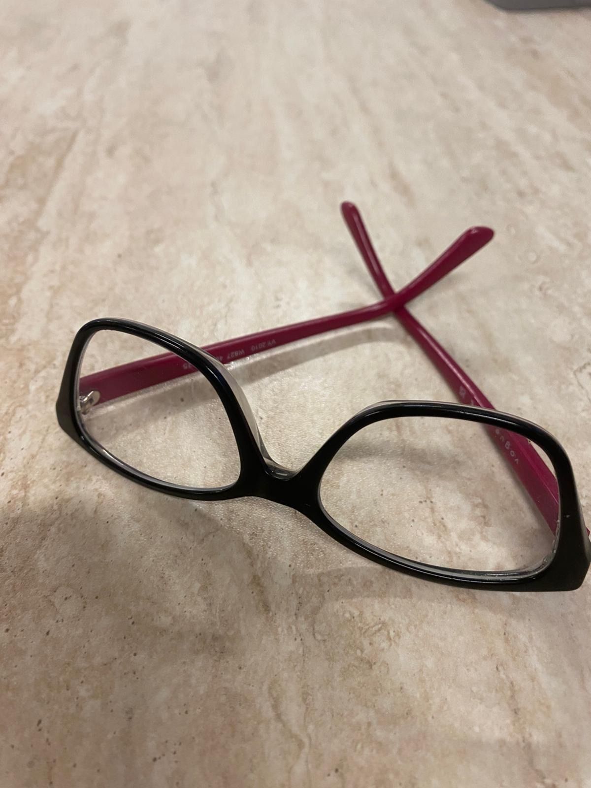 Ein Paar Brille mit roten Bügeln und schwarzen Gläsern liegt auf einer Marmoroberfläche. Die Gläser sind klar und der Bügel hat eine silberne Scharnier.
