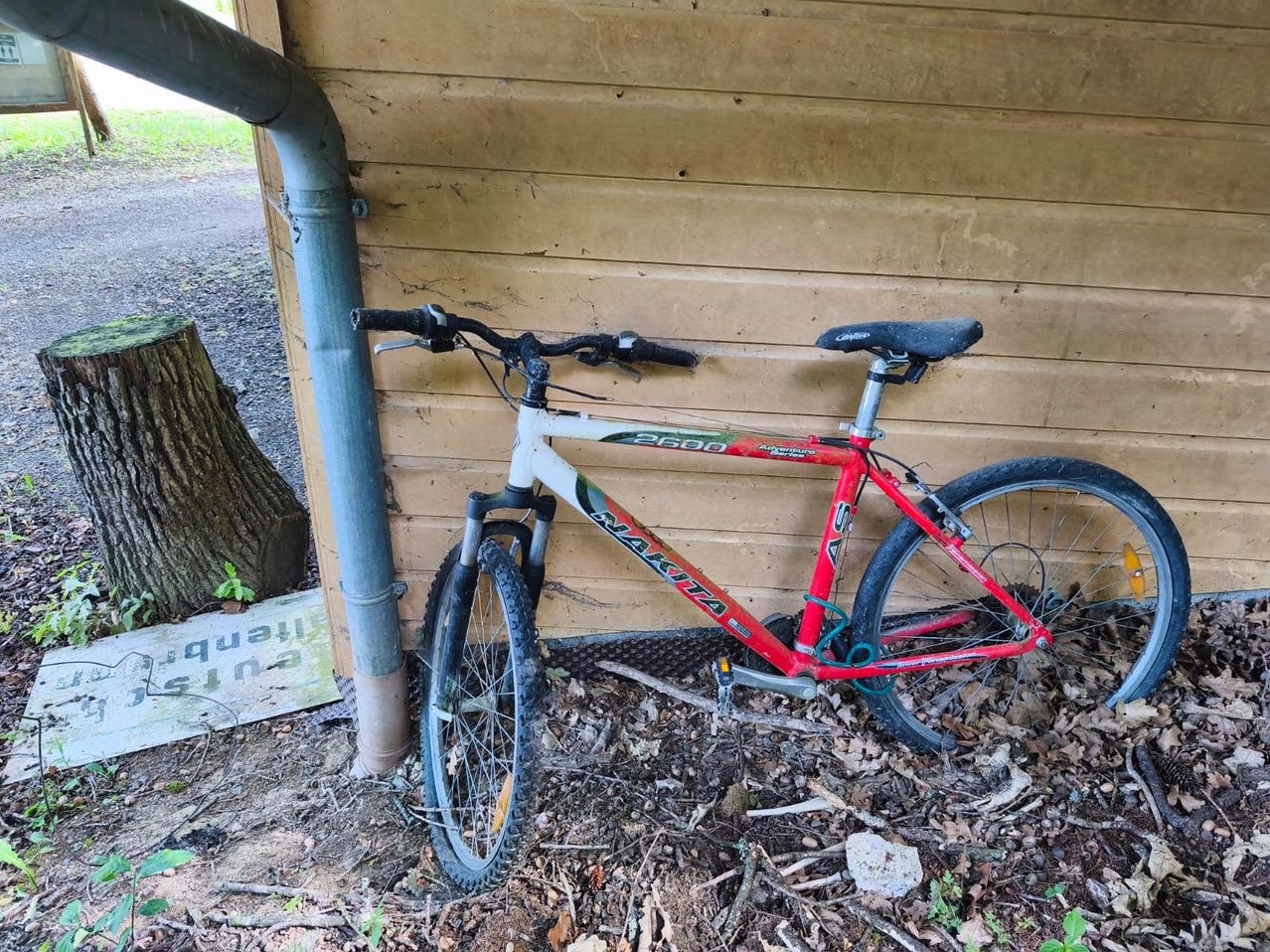 Ein rotes und weißes Mountainbike ist an einer Holzwand geparkt. Das Fahrrad hat einen schwarzen Sattel und einen schwarzen Lenker.