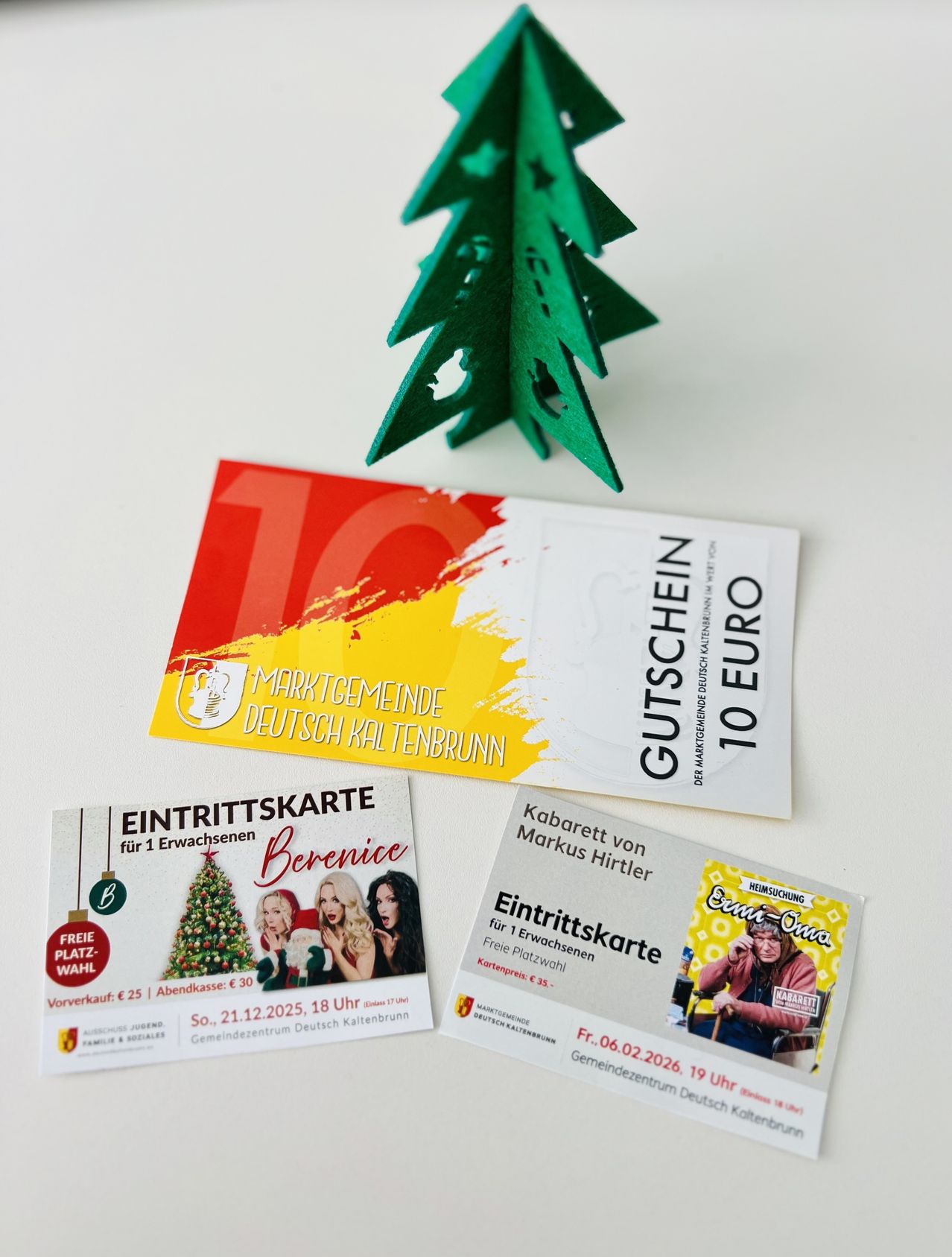 Drei Eintrittskarten für Veranstaltungen im Deutschen Kaltenbrunn Gemeindezentrum werden angezeigt. Ein grüner Papier-Weihnachtsbaum, eine Eintrittskarte für eine freie Wahlveranstaltung am 21. Dezember 2025 und ein Gutschein für 10 Euro.