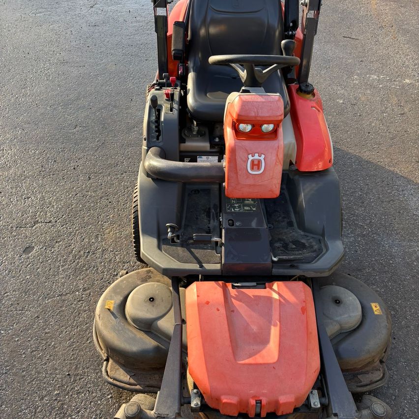 Ein roter und schwarzer Rasenmäher mit Sitz, Lenkrad und zwei großen Rädern steht auf einer Straße.