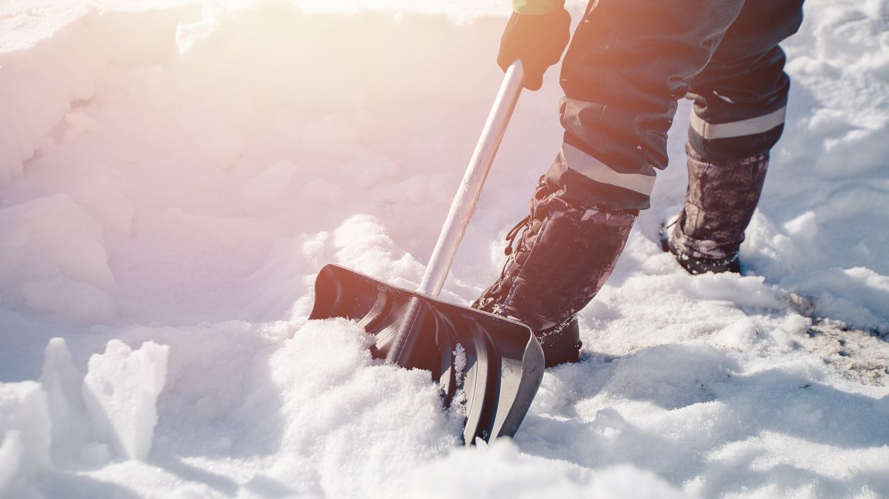 Eine Person in Winterkleidung schaufelt Schnee mit einem Schneeschufel, konzentriert auf die Aufgabe.