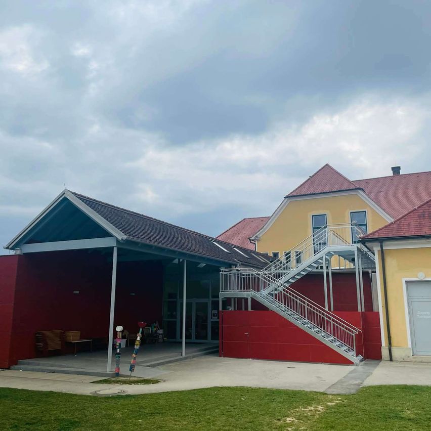 Ein Bild eines modernen Architekturdesigns mit einem roten Gebäude mit rotem Dach, einem weißen Tisch auf der linken Seite und einer Treppe auf der rechten Seite. Der Himmel ist bewölkt.