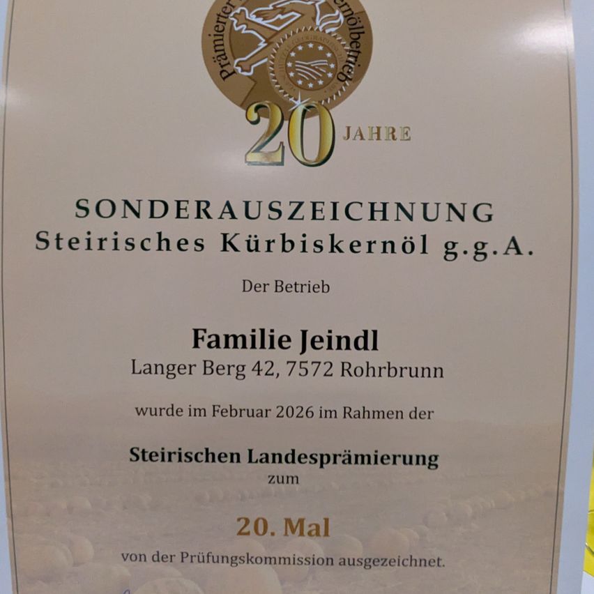 A certificate with golden text '20 Jahre'. It reads 'Sonderauszeichnung Steyrisches Kürbiskernöl g.g.A.' Family Jeindl, Langer Berg 42, 7572 Rohrbrunn, awarded in February 2026 for the Styrian State Award. 20th time from the examination commission.