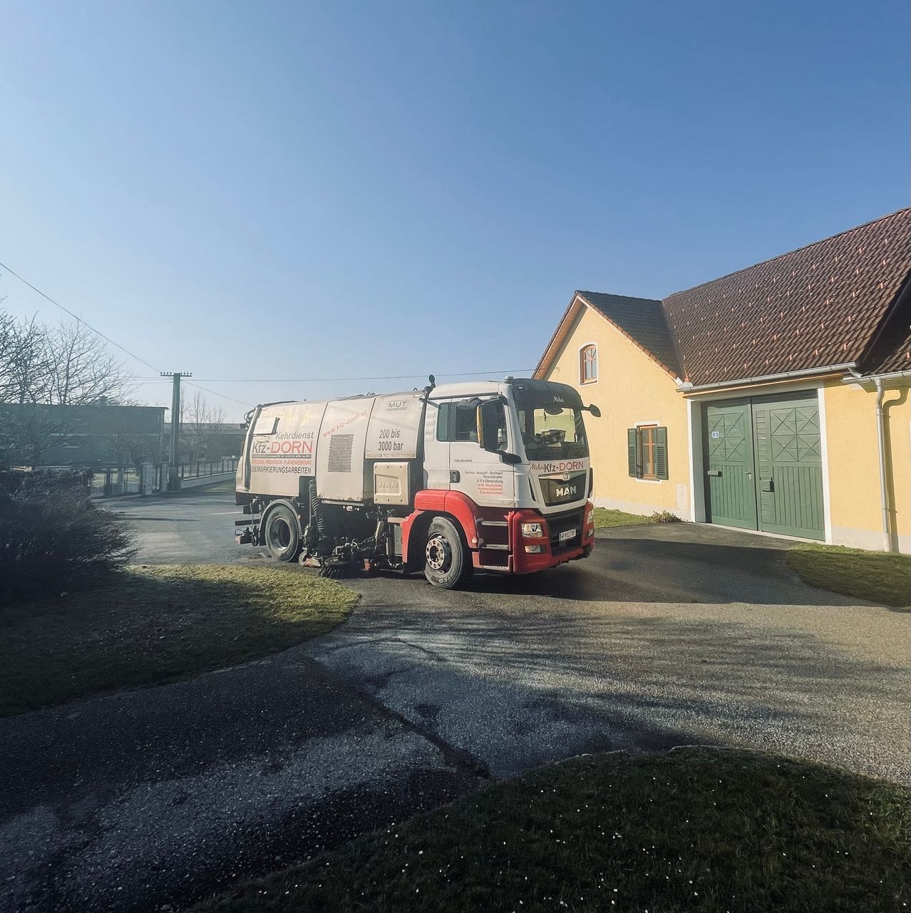 A white and red truck is parked in front of a yellow house with a brown roof and green garage doors.