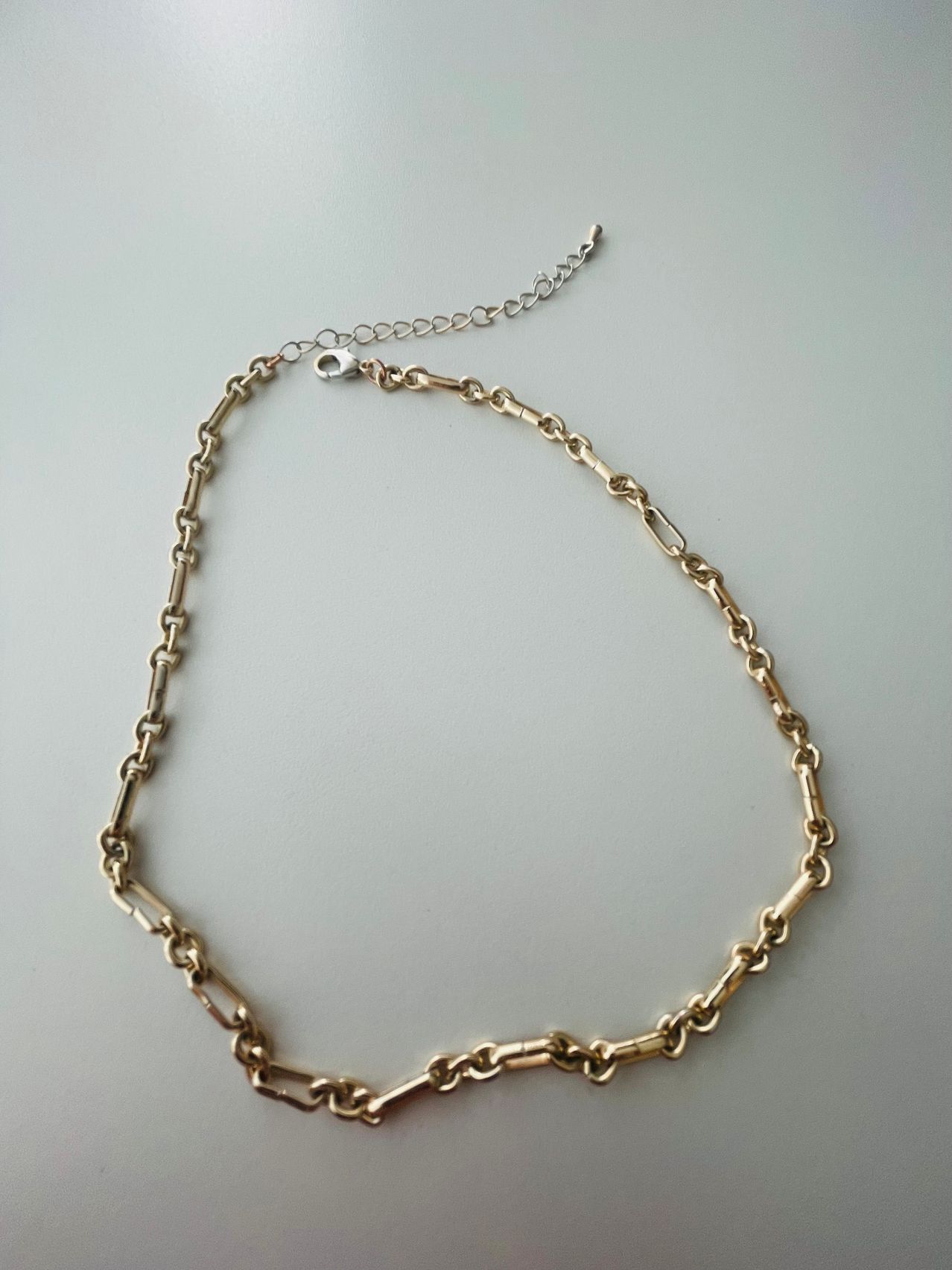 Eine vergoldete Kettenkette wird auf einem hellgrauen Hintergrund gezeigt. Die Kette hat eine Reihe kleiner, rechteckiger Glieder.