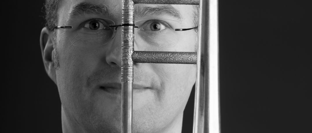 Ein Schwarz-Weiß-Porträt eines Mannes, der ein Posaune vor seinem Gesicht hält.