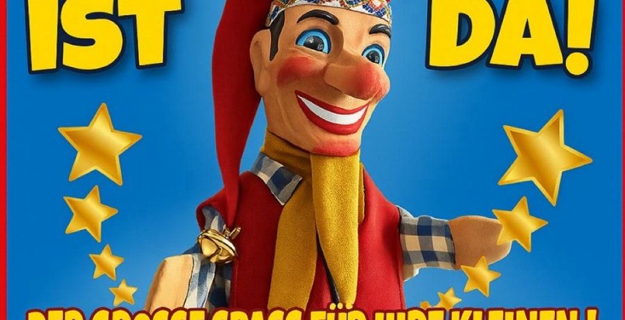 Ein Plakat für eine Puppenshow mit Kasperl, einer fröhlichen Puppe mit rotem Hut und Schal, umgeben von Sternen auf blauem Hintergrund. Der Text lautet 'Kasperl ist da!' und 'Der grosse spass für ihre kleinen!' mit einem gelben Banner darunter.