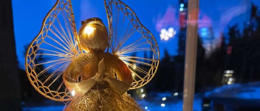 Eine goldene Engelsfigur mit aufwendigen goldenen Flügeln und Lichtern ist auf einer weißen Oberfläche ausgestellt. Sie steht vor einem Fenster mit Nachtaussicht.