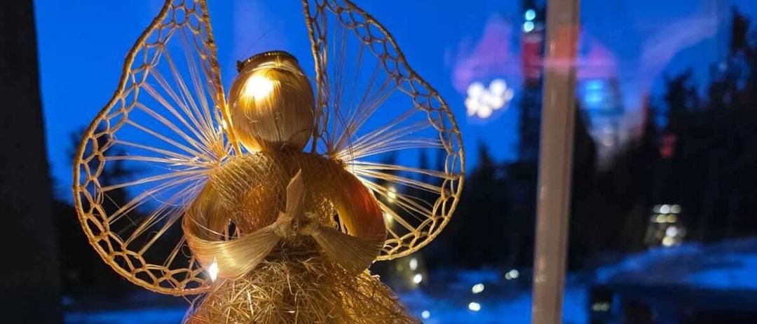 Eine goldene Engelsfigur mit aufwendigen goldenen Flügeln und Lichtern ist auf einer weißen Oberfläche ausgestellt. Sie steht vor einem Fenster mit Nachtaussicht.