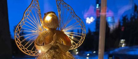Eine goldene Engelsfigur mit Flügeln und leuchtendem Licht steht auf einem Tisch mit einer Girlande aus grünen Lichtern.