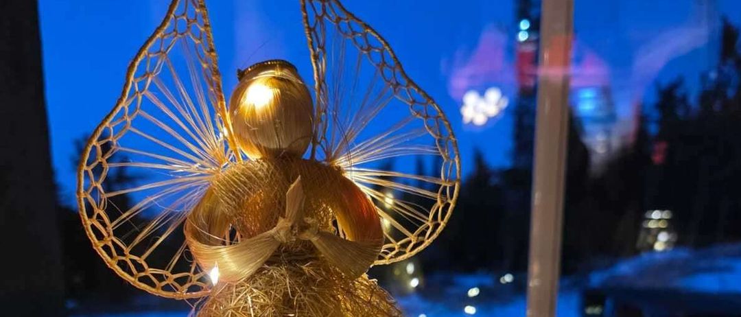 Eine goldene Engelsfigur mit zarten Flügeln und Lichtsträhnen steht auf einer Fensterbank mit Blick auf eine verschneite Landschaft bei Nacht.