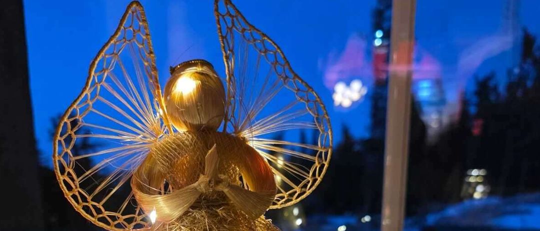 Eine goldene Engel-Dekoration mit Flügeln und Lichtern steht auf einer Fensterbank mit Nachtblick. Ein Kranz mit Lichtern ist in der Nähe.