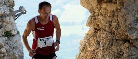 A man in a red shirt with a white number 1 is running through a narrow rocky path.