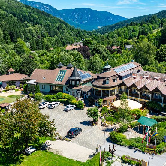 Ein Luftbild eines Hotels, umgeben von üppigen grünen Bäumen und Bergen, mit geparkten Autos vor dem Gebäude.