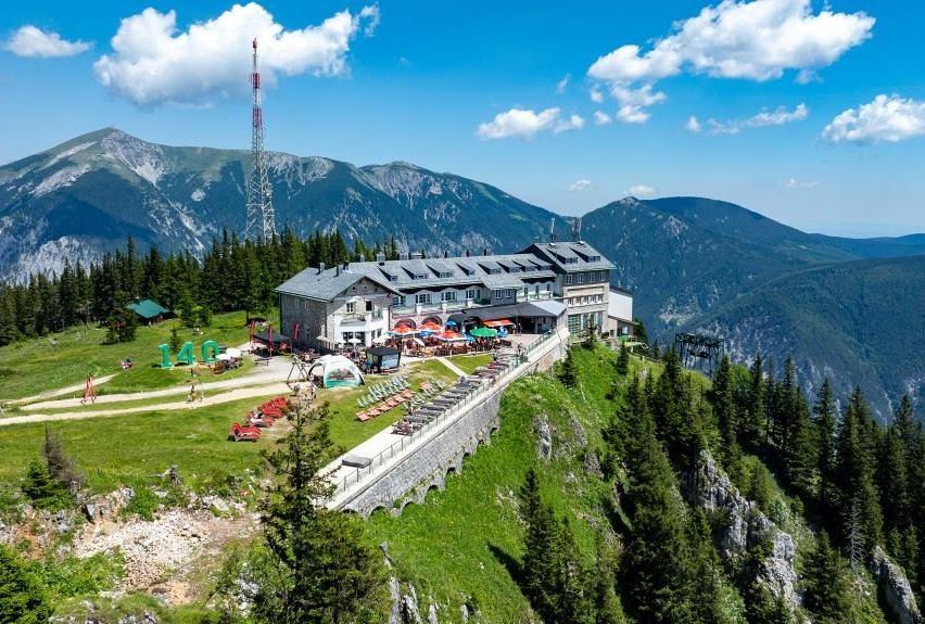 Ein Bergresort mit einem großen Gebäude, zahlreichen Outdoor-Sonnenschirmen und einer malerischen Aussicht auf die umliegenden Berge.