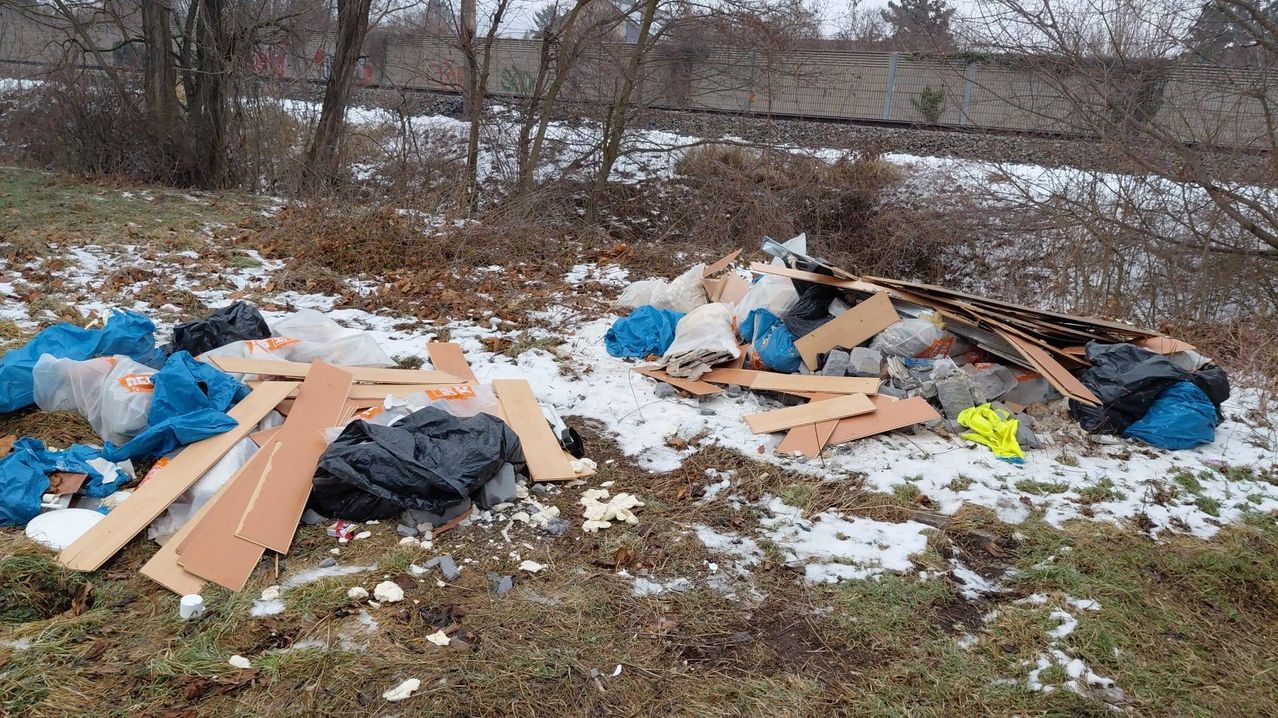 Ein vermüllter Ort, bedeckt mit Schnee, mit verstreuten Plastiktüten, Pappe und anderem Müll in der Nähe eines Zauns.