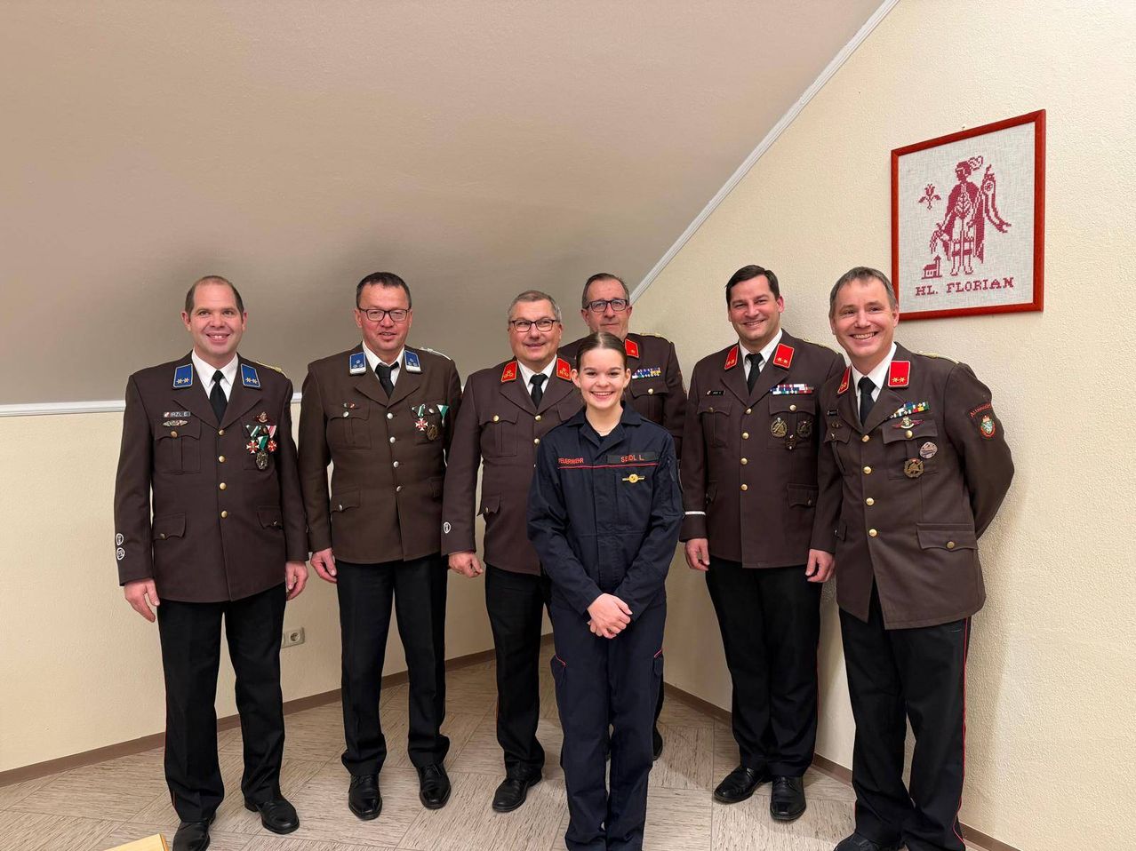 Eine Gruppe von sechs Personen in Militäruniformen, darunter eine Frau in einer anderen Kleidung, stehen zusammen in einem Raum. Sie alle lächeln und scheinen für ein Foto zu posieren.